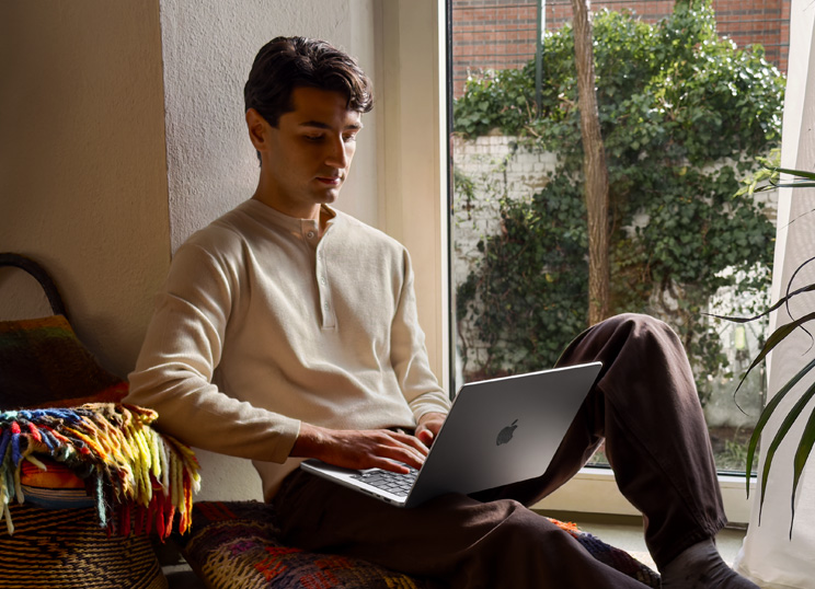 窓際で床に座ってMacBookを使っている人物