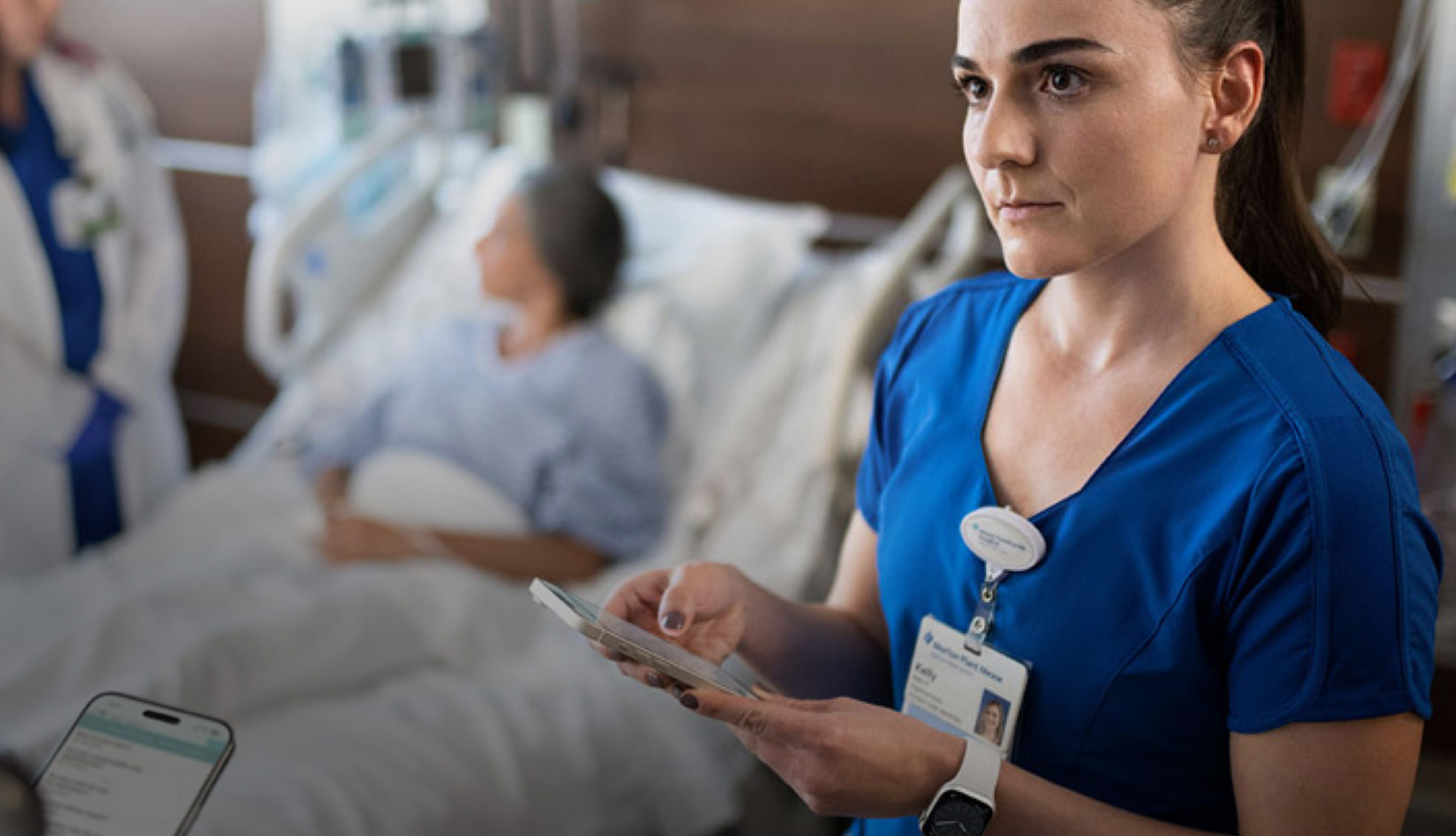 Une infirmière envoie un message sur son iPhone pendant qu’un autre prestataire de soins s’entretient avec une personne hospitalisée.