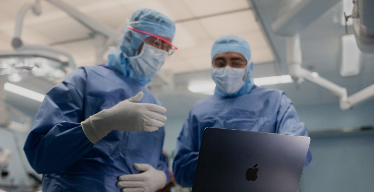 Deux chirurgiens échangent en regardant l’écran d’un MacBook Pro au bloc opératoire.