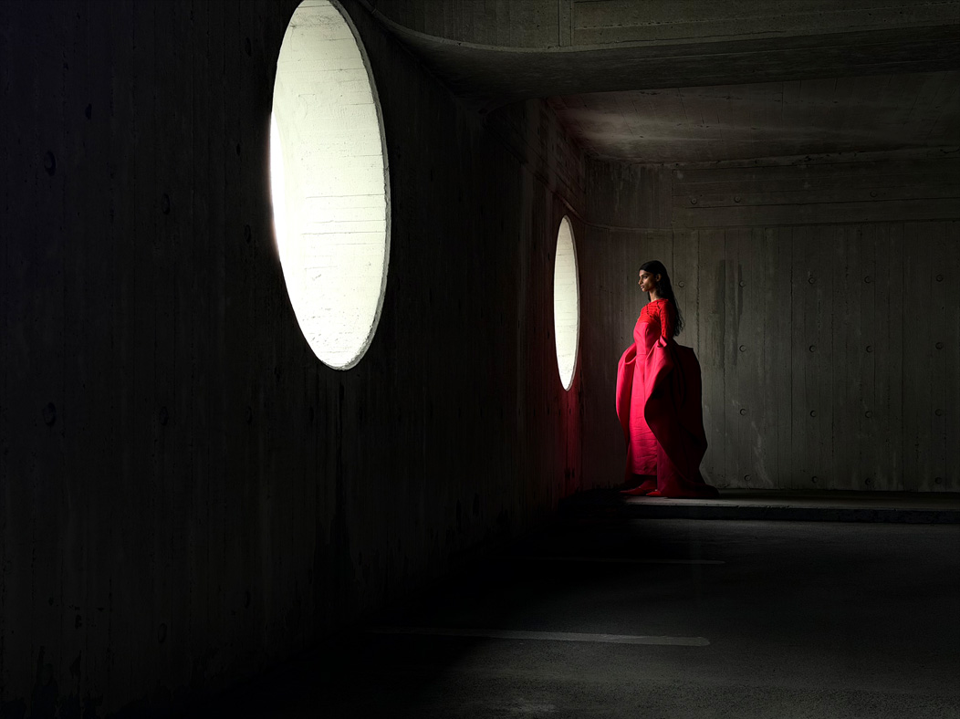 ผู้หญิงใส่ชุดเดรสยาวสีแดงยืนโพสท่าถ่ายภาพอยู่ในห้องว่างๆ แอปรูปภาพสลับเป็นทางยาวโฟกัสช่วงต่างๆ ตั้งแต่ 200 มม. ถึง 13 มม. เพื่อแสดงความสามารถของระบบกล้องระดับโปร